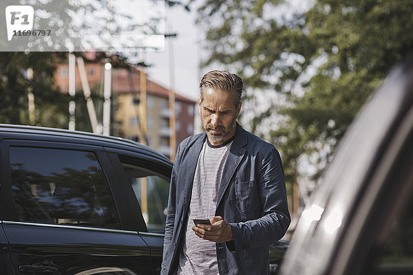 Geschäftsmann  der ein Smartphone benutzt  während er im Park steht.