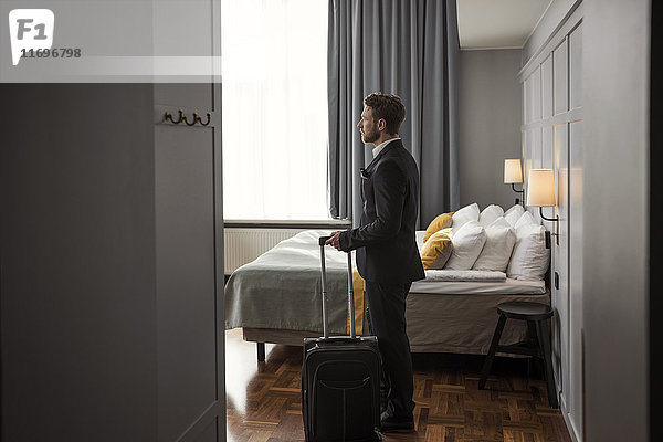 Seitenansicht des Geschäftsmannes mit Gepäck am Bett im Hotelzimmer