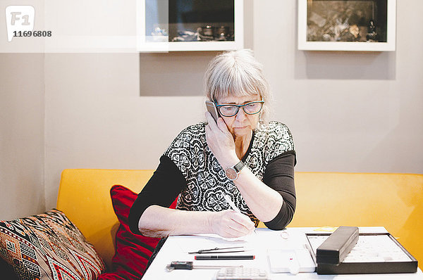 Seniorin beim Telefonieren am Schreibtisch in der Schmuckwerkstatt