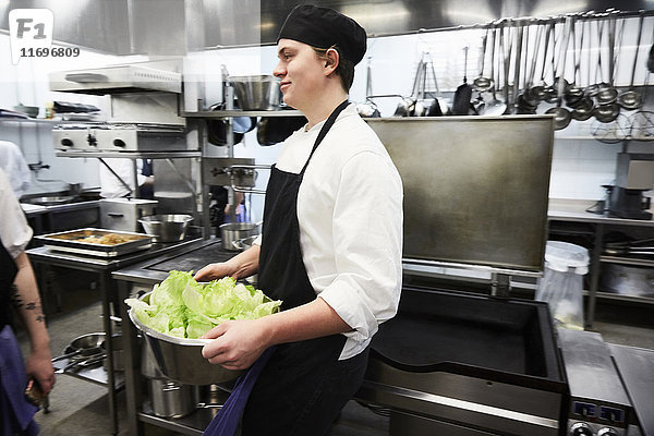 Seitenansicht des männlichen Kochstudenten mit Gemüsebehälter in der Großküche