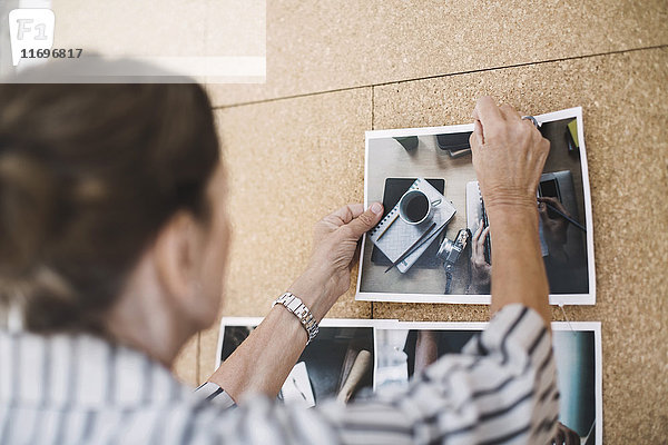 Rückansicht einer älteren Geschäftsfrau  die ein Foto auf einer Pinnwand in einem tragbaren Bürotransporter festhält.
