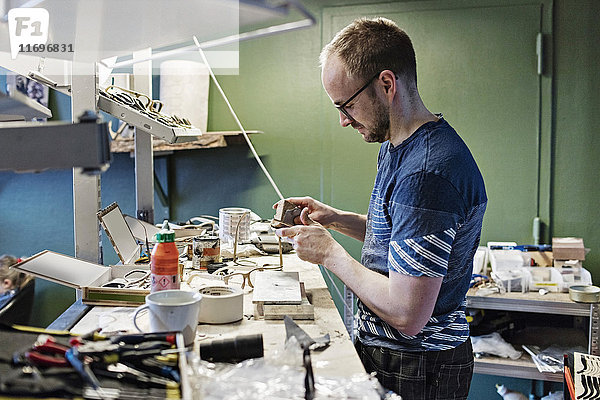 Seitenansicht des männlichen Besitzers bei der Arbeit am Schreibtisch in der Brillenwerkstatt