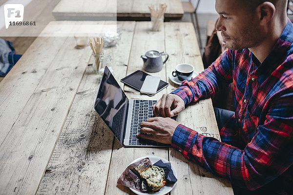 Seitenansicht eines erwachsenen Mannes mit Laptop am Tisch im Coffee Shop