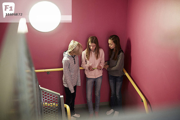 Mädchen mit Handy mit Freunden gegen rosa Wand in der Mittelschule