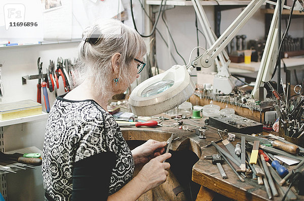 Seitenansicht der Seniorin bei der Schmuckherstellung an der Werkbank in der Werkstatt