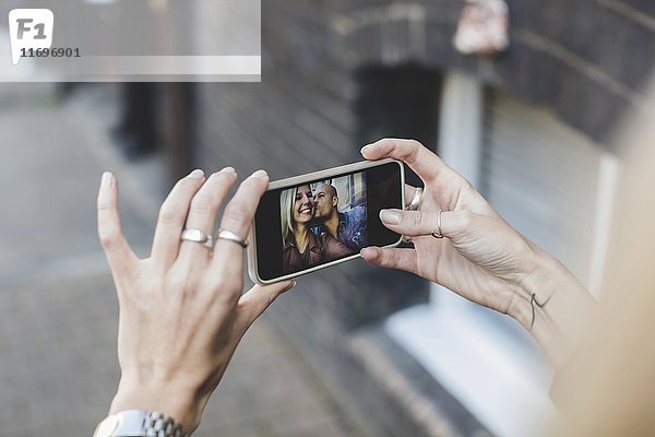 Mann küsst Frau  wie sie Selfie durch Smartphone nimmt