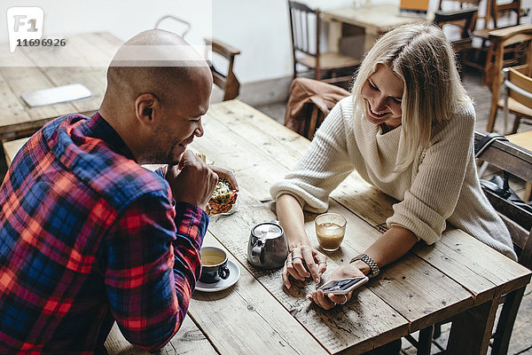 Multiethnisches Paar mit Handy am Tisch im Coffee-Shop