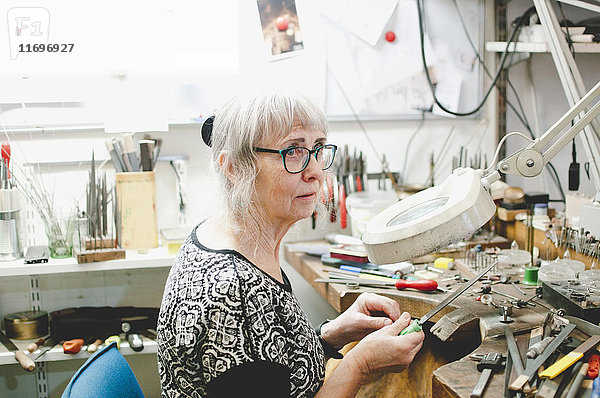 Senior Handwerker schaut weg  während er in der Werkstatt Schmuck herstellt.