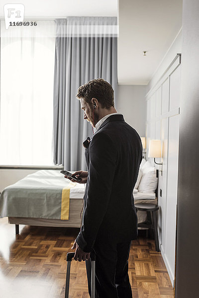 Seitenansicht des Geschäftsmannes mit Handy und Gepäck im Hotelzimmer