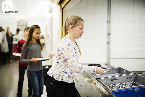 Mädchen stellen Teller in Kiste nach dem Mittagessen in der Schulcafeteria