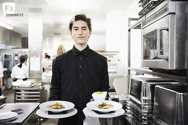 Porträt eines selbstbewussten Kellners mit Geschirr in der Großküche