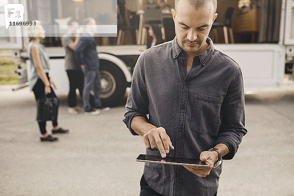 Geschäftsmann mit digitalem Tablett mit Kollegen und tragbarem Office-Truck auf der Straße im Hintergrund