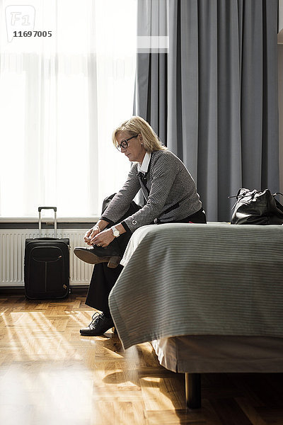 Seitenansicht der Geschäftsfrau beim Schnürsenkelbinden auf dem Bett im Hotelzimmer