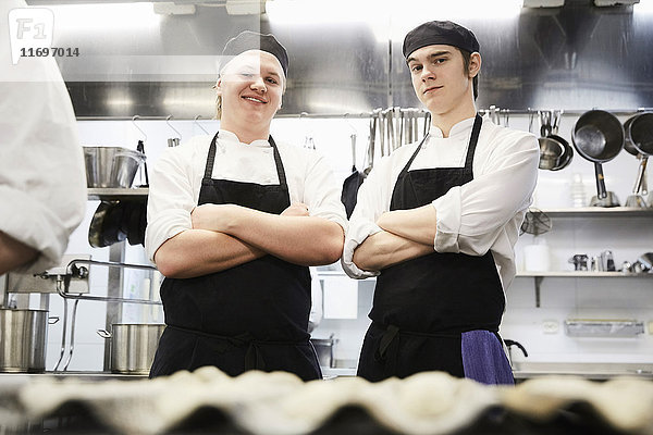 Porträt von lächelnden männlichen Kochstudenten  die in der Großküche gekreuzt stehen.