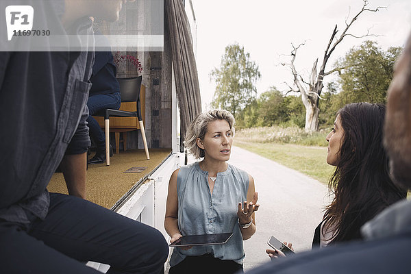 Geschäftsfrau mit digitalem Tablett im Gespräch mit Kollegen per tragbarem Bürowagen