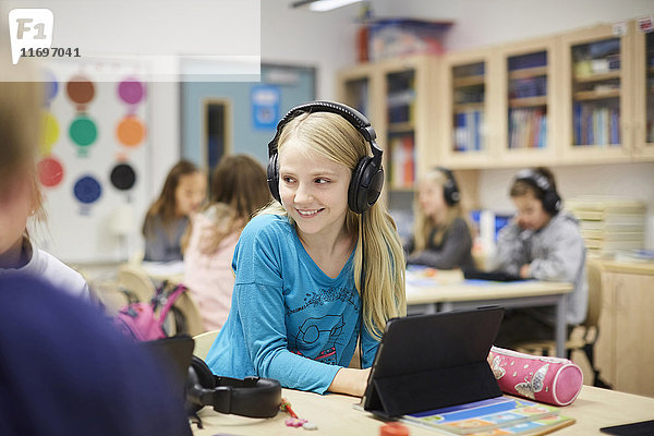 Lächelndes Mädchen mit Kopfhörern bei der Benutzung des digitalen Tisches im Klassenzimmer