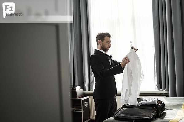 Seitenansicht des Geschäftsmannes mit weißem Hemd im Kleiderbügel im Hotelzimmer