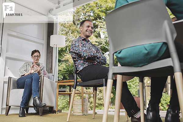 Geschäftsfrau mit Smartphone  während Kollegen auf Stühlen im tragbaren Bürowagen sitzen