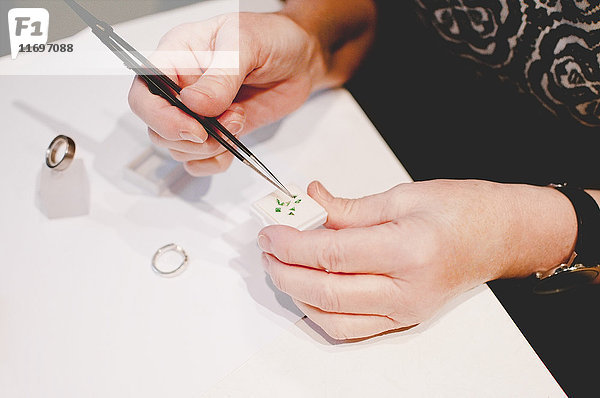 Abgeschnittenes Bild einer älteren Handwerkerin  die in der Werkstatt Schmuck zusammenbaut