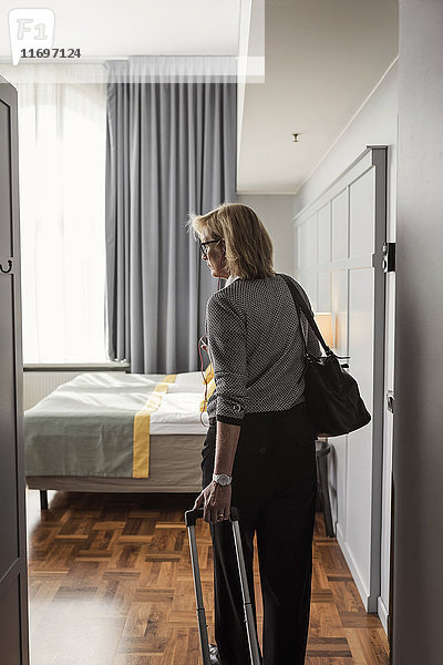 Rückansicht der Geschäftsfrau mit im Hotelzimmer stehendem Gepäck