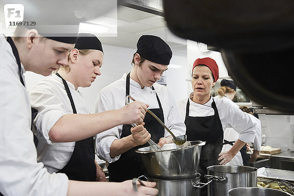 Lehrer assistiert männlichen Schülern beim Kochen von Lebensmitteln in der Großküche