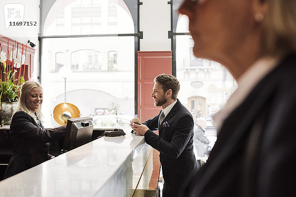 Glücklicher Geschäftsmann im Gespräch mit Empfangsdame an der Hotelrezeption