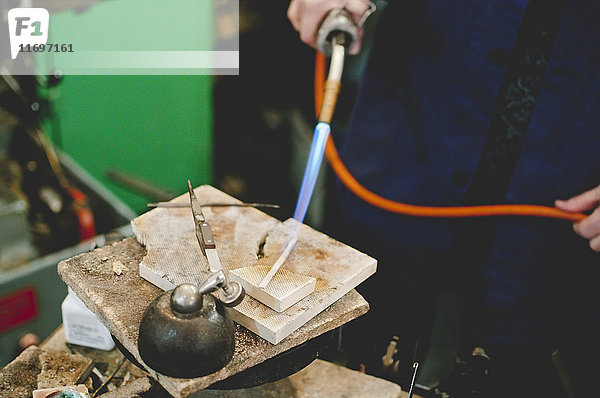 Mittelteil eines älteren Handwerkers  der eine Lötlampe für die Metallbearbeitung in der Schmuckwerkstatt einsetzt