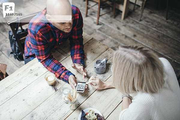 Hochwinkelansicht eines multiethnischen Paares mit Handy im Coffee-Shop