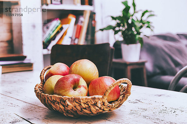 Korb mit Äpfeln auf Holztisch im Wohnzimmer