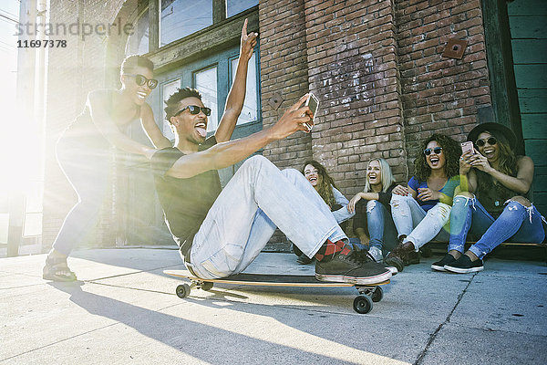 Frau schiebt Freund auf Skateboard sitzend in der Stadt