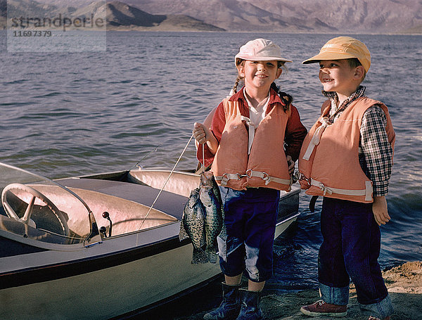 Porträt eines kaukasischen Bruders und einer Schwester  die mit Fischen in der Nähe eines Bootes posieren