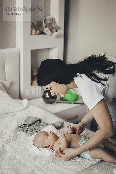 Kaukasische Mutter wechselt die Windel ihres kleinen Sohnes im Bett