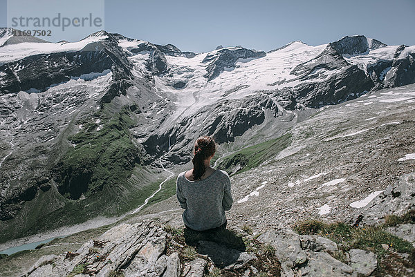 Kaukasische Frau sitzt auf einem Felsen und bewundert die schöne Aussicht auf einen Berg