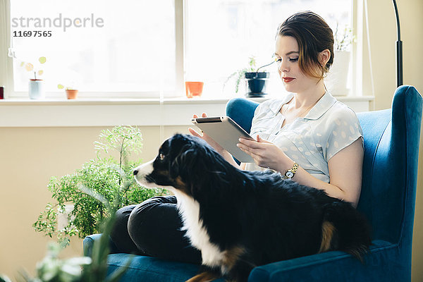 Frau im Sessel sitzend mit Hund und digitalem Tablet