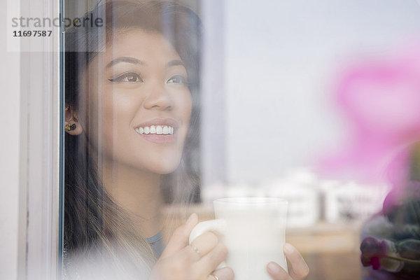 Mixed Race Frau trinkt Kaffee hinter Fenster