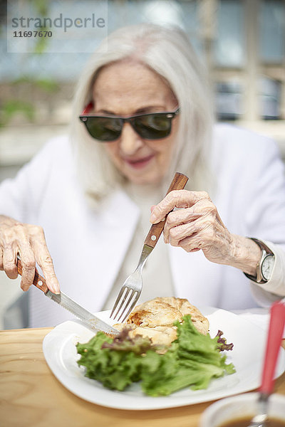 Ältere kaukasische Frau schneidet Essen auf dem Teller