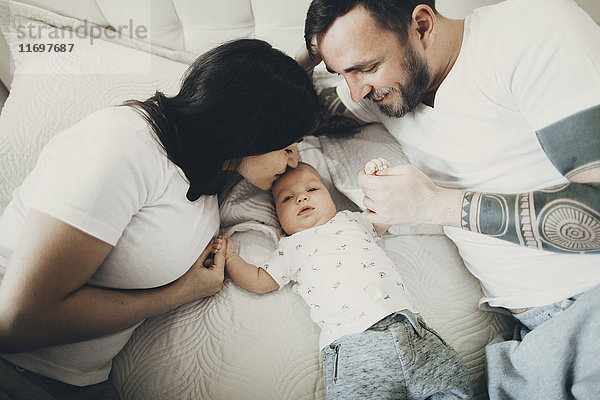 Kaukasische Mutter und Vater halten Hände mit Baby Sohn auf Bett