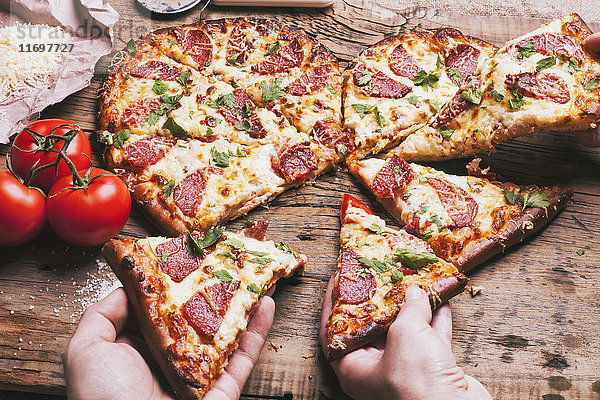 Hände  die herzförmige Pizzastücke in die Nähe der Zutaten auf dem Schneidebrett ziehen