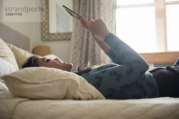 Gemischtrassige Frau auf dem Bett liegend mit digitalem Tablet