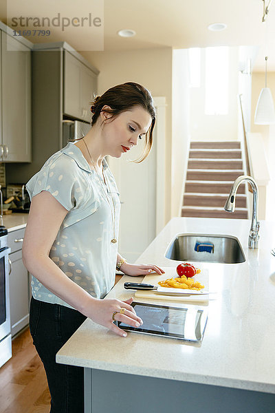 Frau  die ein digitales Tablet benutzt und Lebensmittel in der heimischen Küche zerkleinert