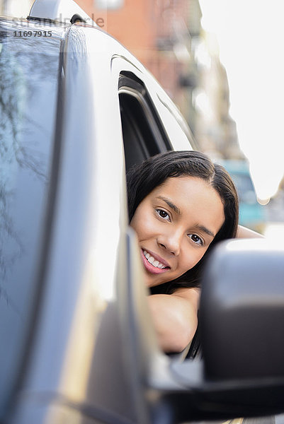 Porträt einer hispanischen Frau  die sich aus dem Autofenster lehnt