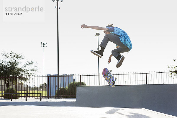 Hispanischer Mann  der einen Trick in der Luft auf einem Skateboard vorführt