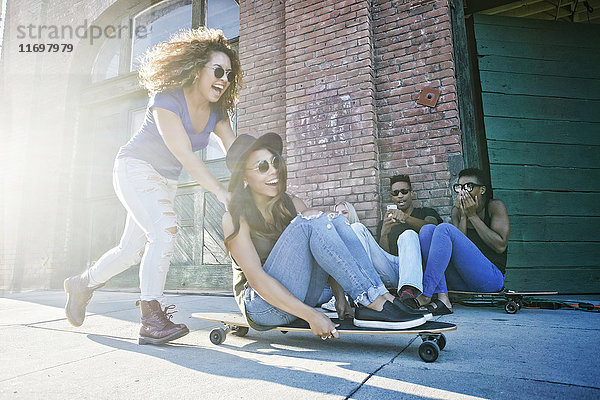 Frau schiebt Freund auf Skateboard sitzend in der Stadt