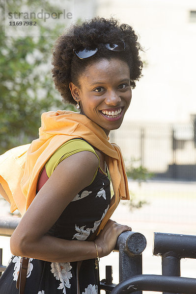 Porträt einer lächelnden afroamerikanischen Frau  die sich an ein Geländer lehnt