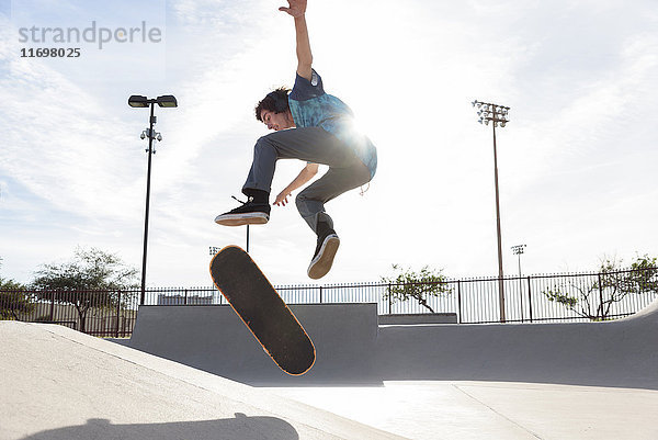 Hispanischer Mann  der einen Trick in der Luft auf einem Skateboard vorführt