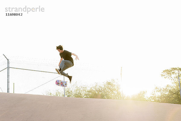 Hispanischer Mann  der einen Trick in der Luft auf einem Skateboard vorführt