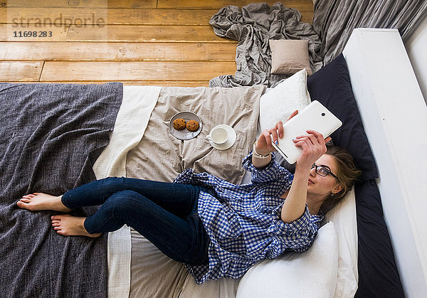 Kaukasische Frau  die auf dem Bett liegt und für ein Selfie mit einem digitalen Tablet posiert