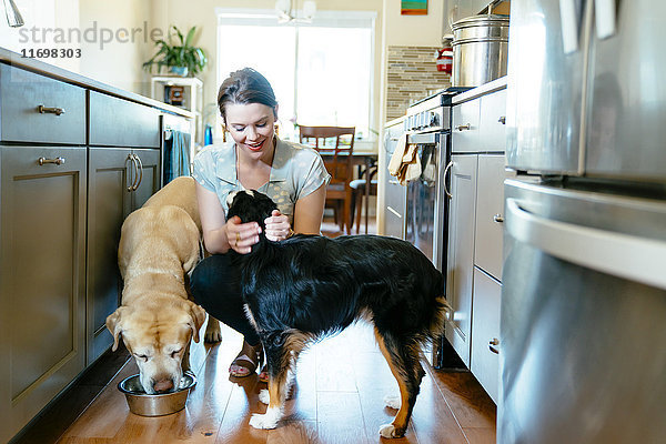 Frau füttert und streichelt Hunde in häuslicher Küche