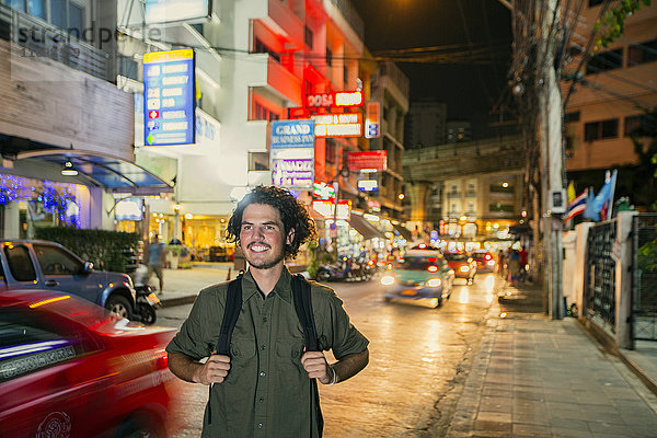 Lächelnder Mann mit Rucksack in der Stadt bei Nacht