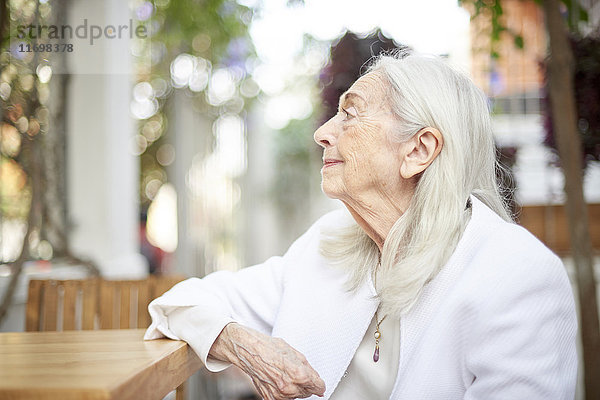 Profil einer lächelnden älteren kaukasischen Frau  die am Tisch sitzt